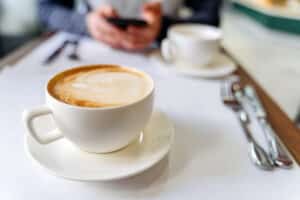 kop med kaffe på bordet i en kaffebar. mand bruger en telefon i baggrunden