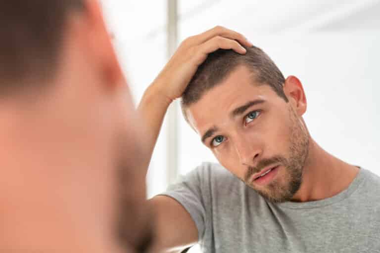 jauns vīrietis pārbauda matus spogulī